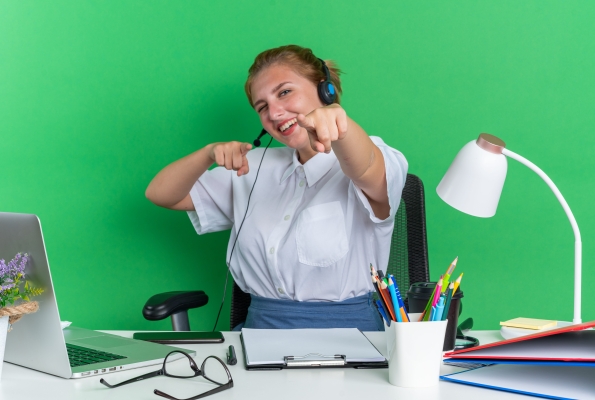 0001_joyful-young-blonde-call-centre-girl-wearing-headset-sitting-desk-with-work-tools-winking-doing-you-gesture_1785475832-7974cfaa3d9256e21fc9a0a4e231460c.jpg